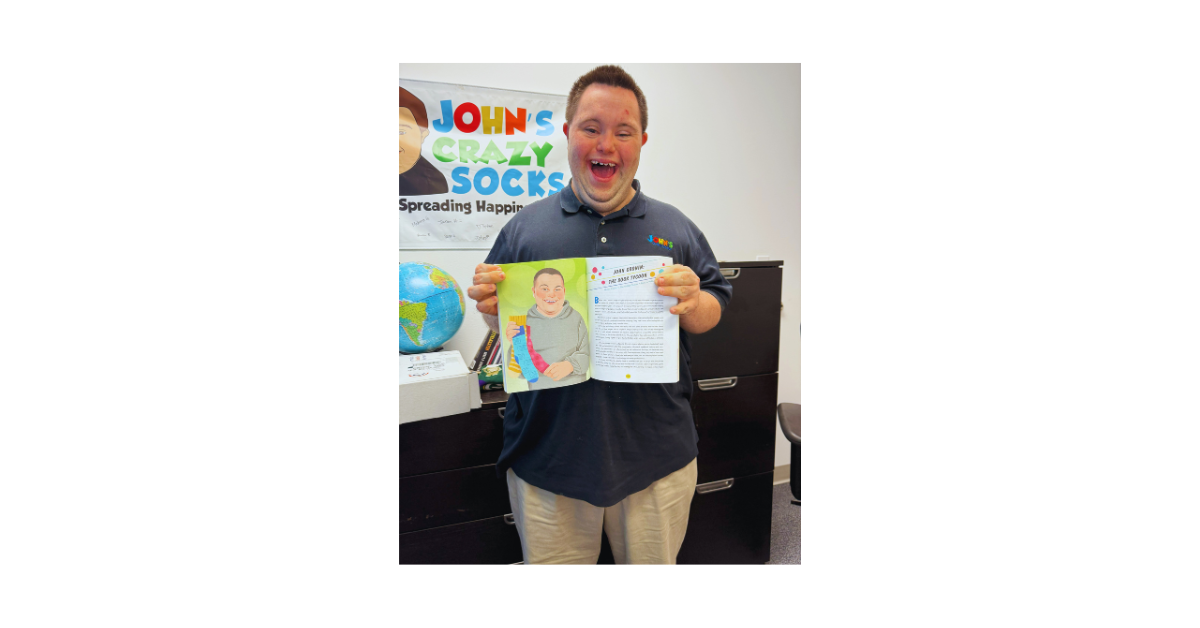 John Cronin, co-founder of John’s Crazy Socks, smiles proudly while holding his featured chapter in Down Syndrome Out Loud by Melissa Hart.