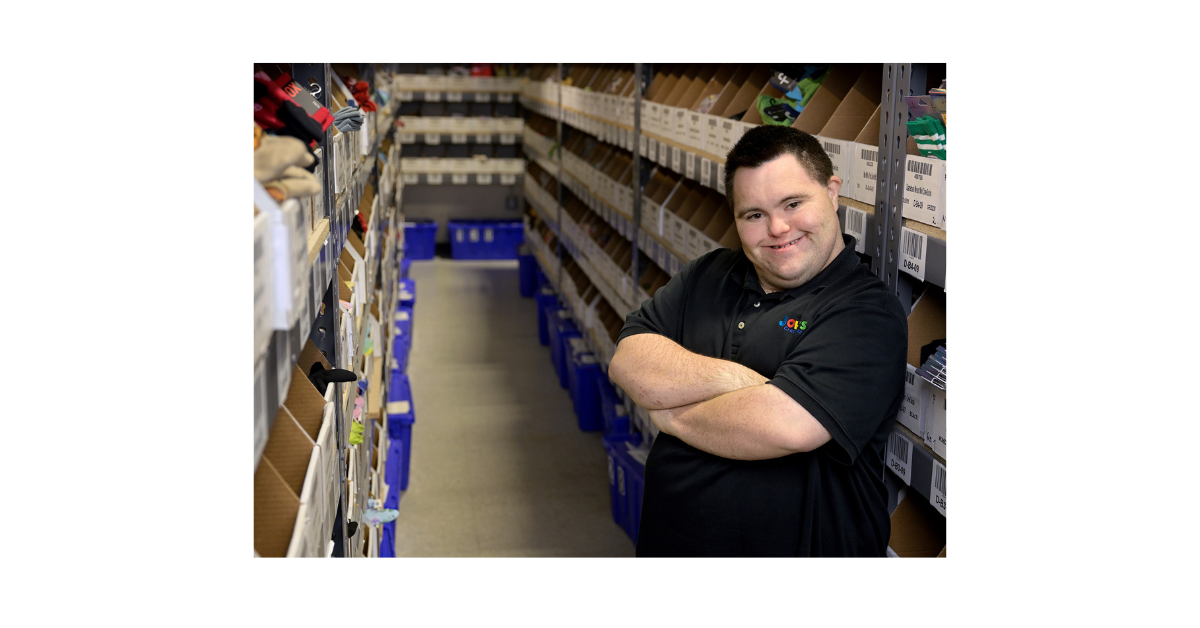 John Cronin stands proudly in the warehouse, surrounded by rows of colorful socks.