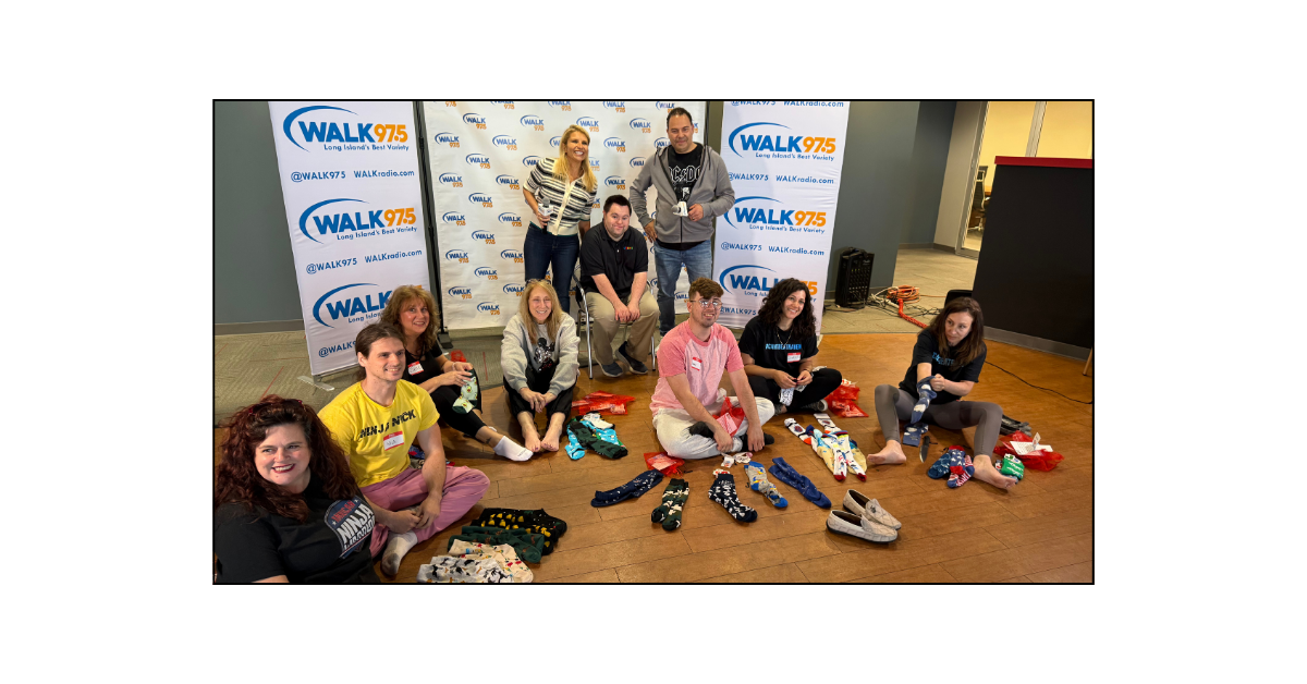 Hosts Anna and Raven pose with contestants before the Sock Smackdown at WALK 97.5, surrounded by colorful socks from John’s Crazy Socks.