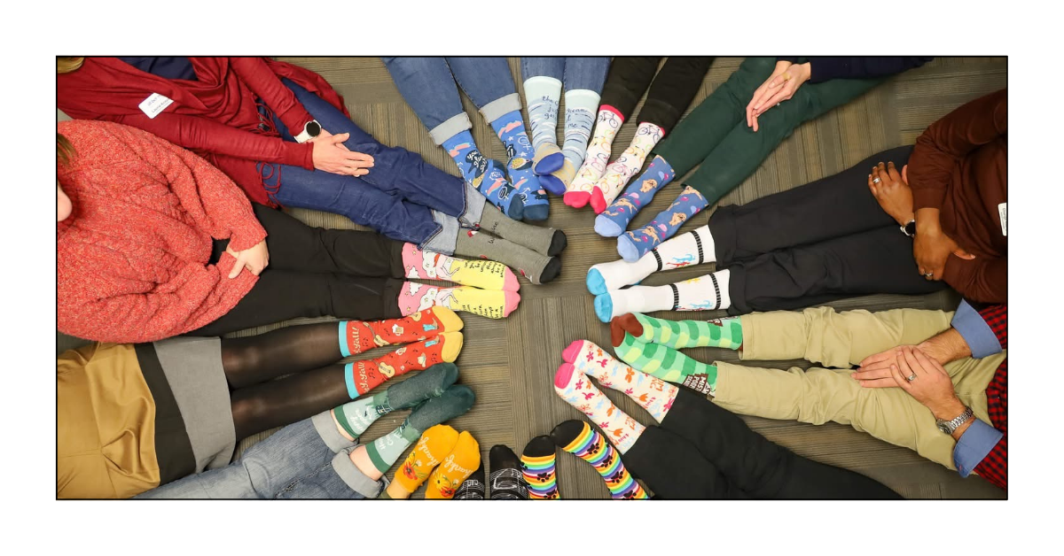 Customers sitting in a circle, showing off colorful socks from John’s Crazy Socks for World Down Syndrome Day.