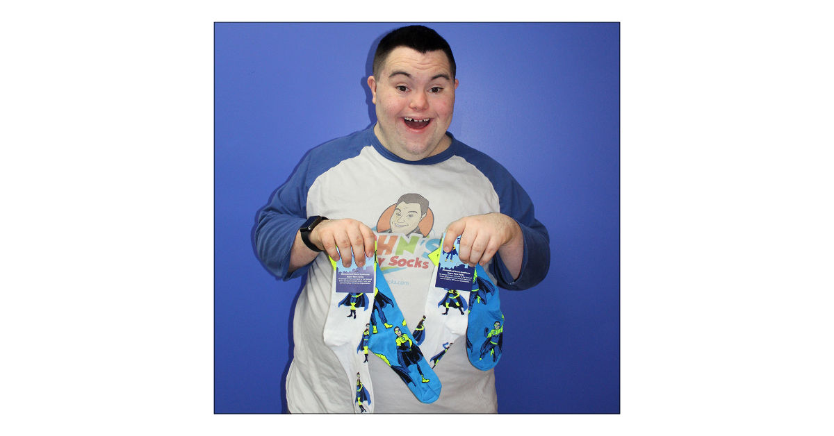 John Cronin holding 2 pairs of the Down Syndrome Superhero Crew Socks.  