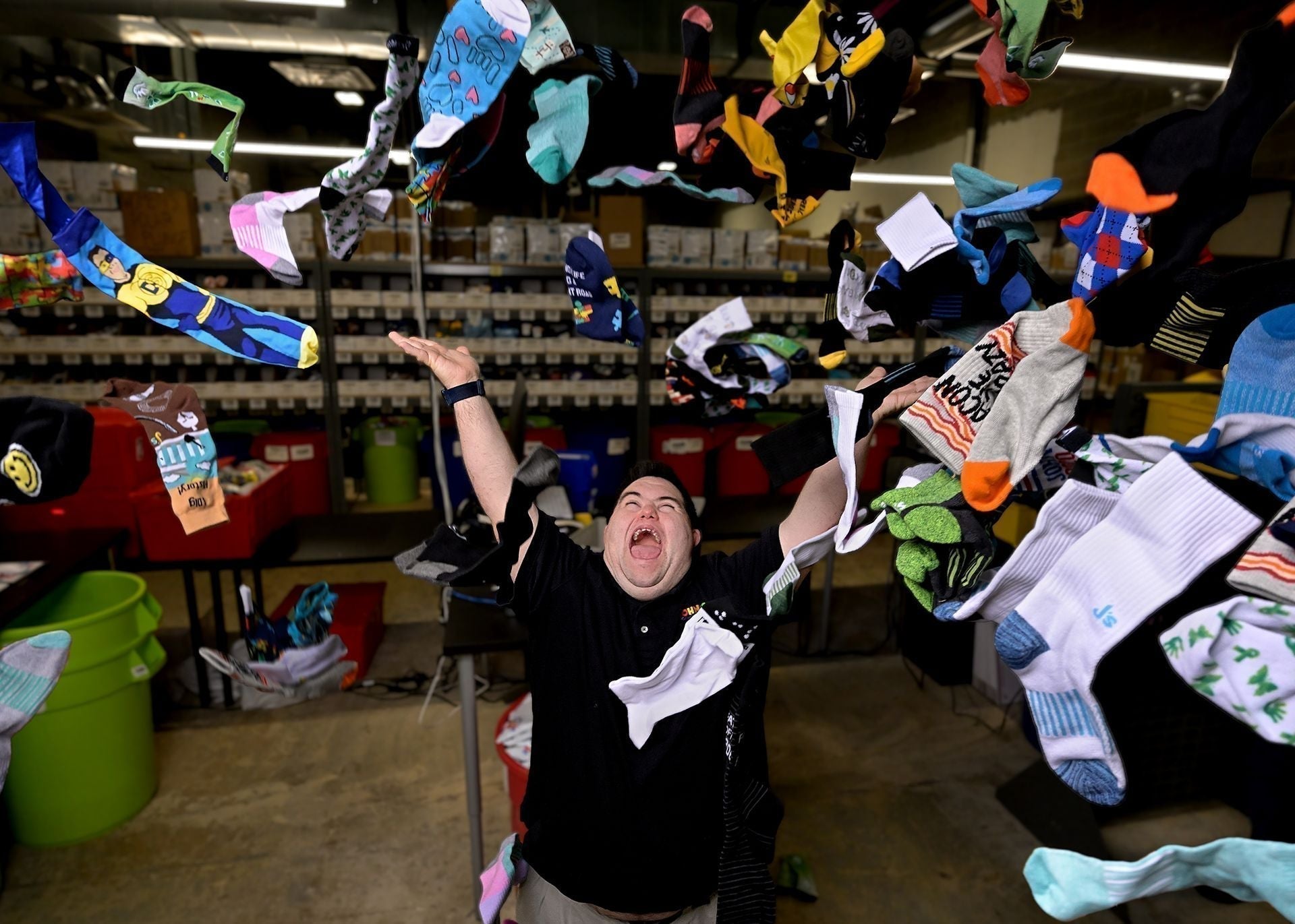 John Cronin, co-founder of John’s Crazy Socks, happily throws colorful socks in the air in a busy warehouse.